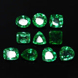 Translucent green emerald lot placed on black surface, with diverse shapes reflecting the expert cut and natural heat treatment.