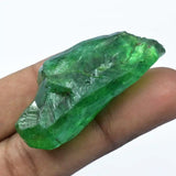Green crystal held between fingers against a white background
