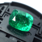 Natural Muzo 10.90 carat square cushion emerald displayed on black plastic surface for texture contrast.