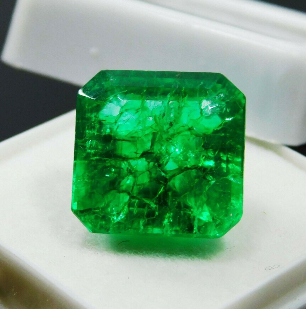 Certified natural Colombian emerald of 7 carats placed in a white display box, highlighting its vivid green color and excellent emerald cut.