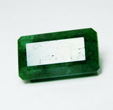 A brilliant 24.65 carat certified natural Colombian emerald with emerald cut, lying horizontally on a white background, showcasing its eye-clean clarity and rich green color.