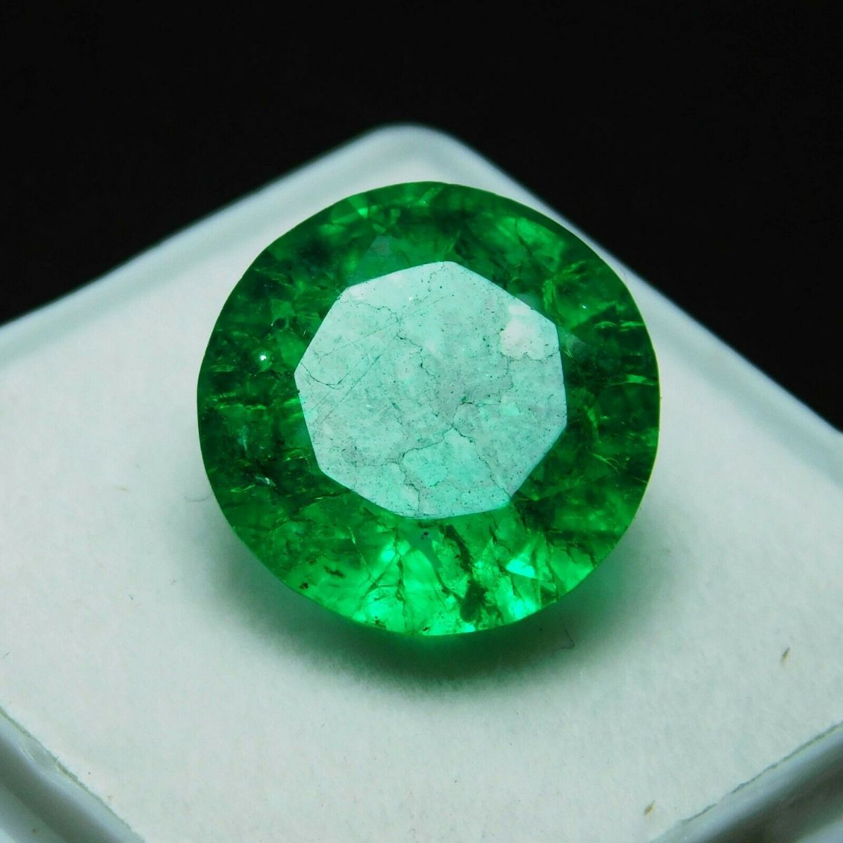 8.23 carat round cut Colombian emerald placed inside a white square case with a black background, highlighting the gem's vivid green color and precision cut.