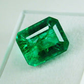 Certified 10.63 carat natural green emerald placed on a white surface, showcasing its vivid emerald cut and deep green color.