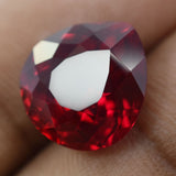 Pear cut natural red ruby held between two fingers with green leaves in background – 8.65 Ct