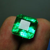 Dimmer view of the emerald held in fingers, revealing internal characteristics and natural inclusions.