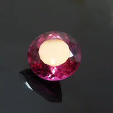 Pink gemstone on a black stand against a dark background