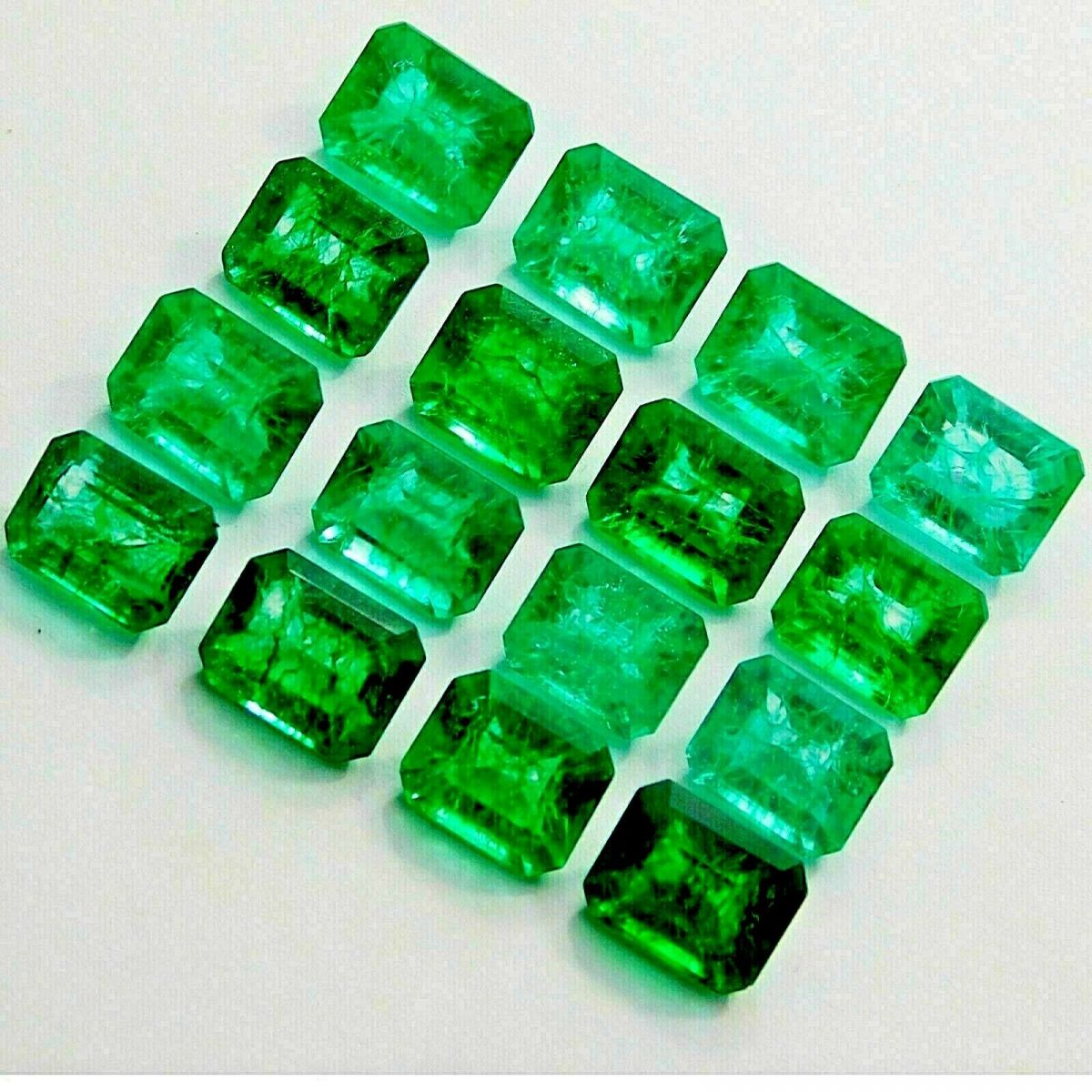Certified green emerald gemstones arranged in neat rectangular rows on white background