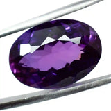 Purple gemstone held between two metal prongs on a white background