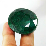 Big oval-shaped green emerald placed between fingers, displaying its clarity and smooth surface