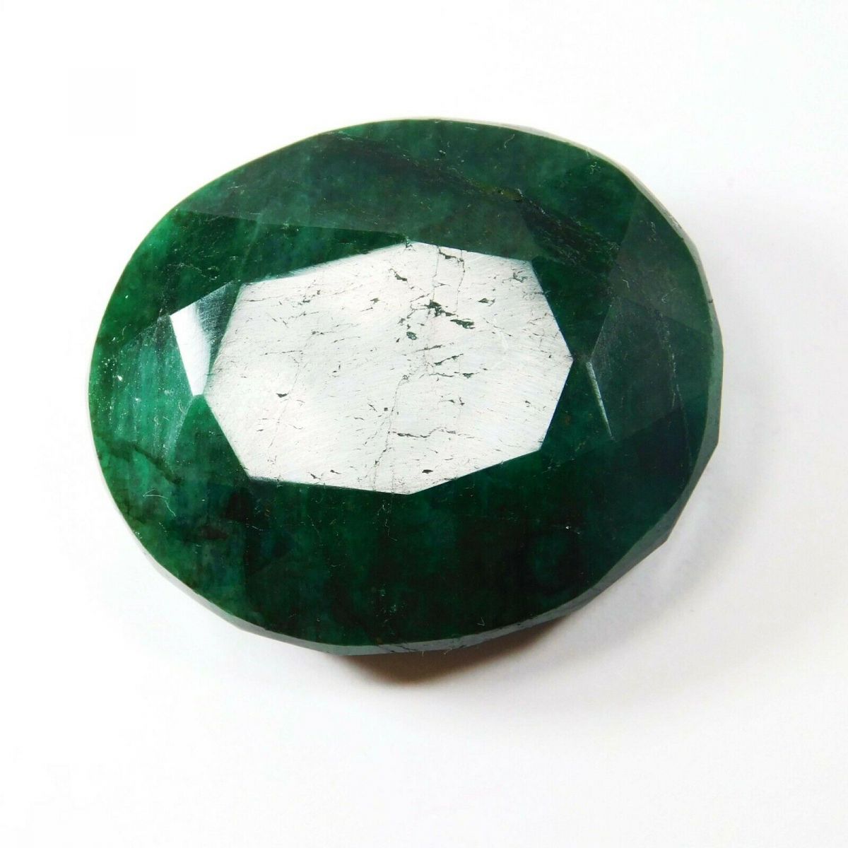 Large green oval emerald reflecting light at center, placed on neutral background highlighting its vibrant color