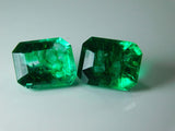 Zoomed-out view of natural emerald gemstone pair placed on flat surface, showing reflection and symmetry of cut