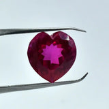 Heart-shaped red gemstone held by tweezers against a light blue background