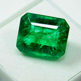 Close-up of natural emerald cut gemstone placed on white tiled background, rich green color and excellent clarity