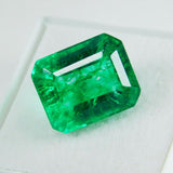 Emerald gemstone placed flat on white surface, translucent green color with clarity-enhanced finish