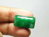 24.65 carat green Colombian emerald held delicately between two fingers, illustrating its actual size, excellent cut, and natural asterism effect under light.