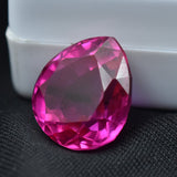 Certified pear-shaped pink ruby resting on black surface beside a white box