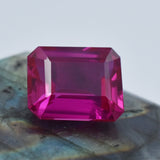 Natural pink ruby emerald cut shown on elegant neutral-toned surface