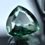 Trillion-cut green gemstone on a reflective surface with a blurred background