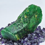 Green emerald rough stone on blue background – uncut gemstone