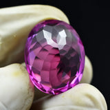 Faceted purple gemstone held by a gloved hand against a black background