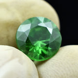 4.95 Ct Green Tsavorite Garnet held between two gloved fingers, round cut, translucent and eye-clean