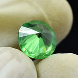 Flipped round cut 4.95 Ct Green Garnet held by gloved fingers, clarity enhanced and certified gemstone