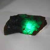 “Raw green gemstone with a bright internal glow, displayed on a white surface.”