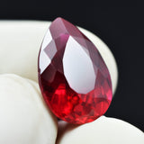 Natural red ruby held between three gloved fingers showing brilliant pear cut
