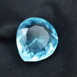 “Sparkling blue faceted gemstone resting on black textured fabric.”