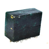 “Raw rectangular green crystal chunk displayed over scattered purple rough stones.”