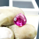 Natural pink ruby pear cut gemstone held between gloved fingers for close inspection