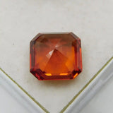 Faceted red-orange gemstone on a light beige background