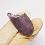 Amethyst crystal held in a hand against a white background