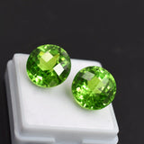 Two green gemstones on a white stand with a dark background