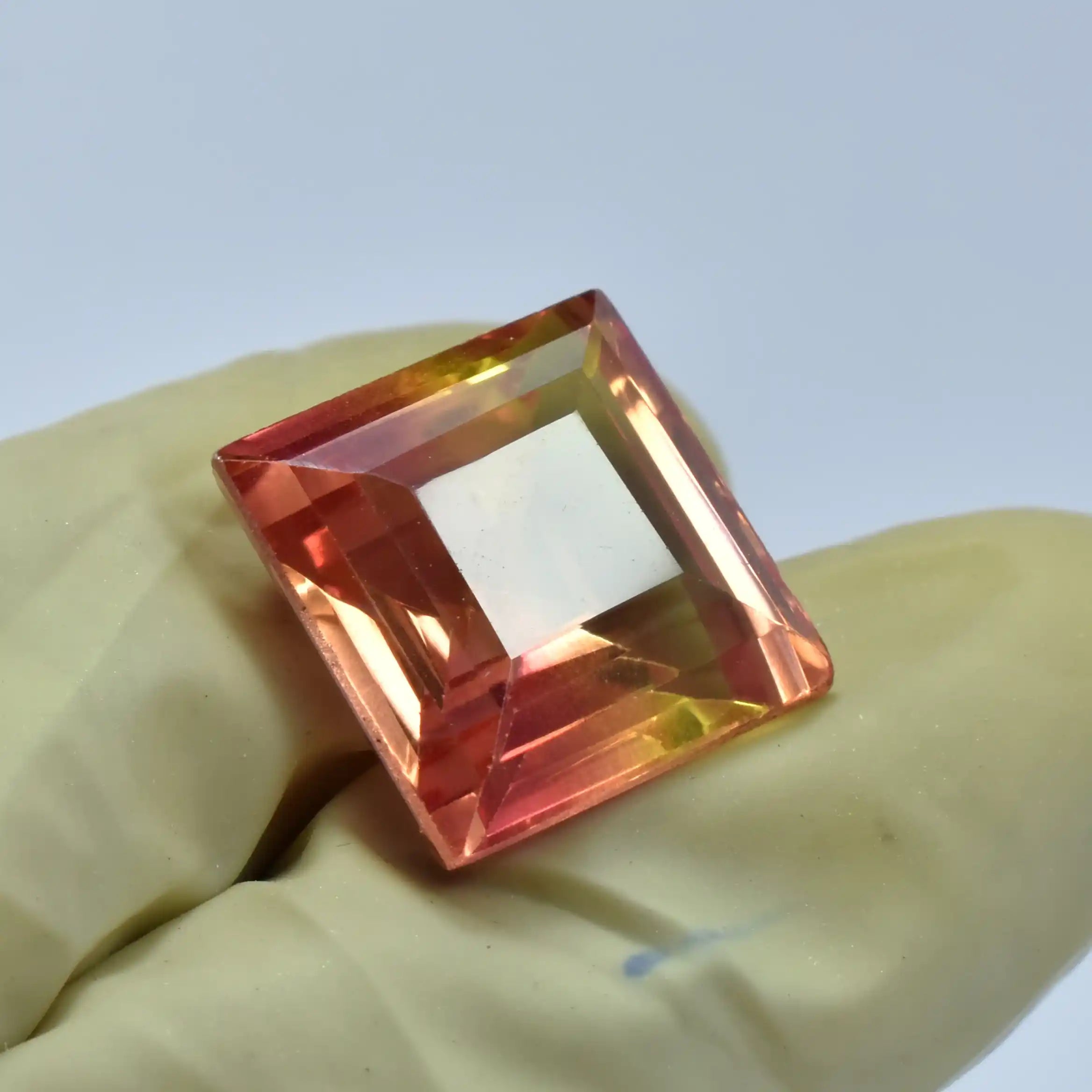 Square-cut gemstone held by a gloved hand against a light blue background