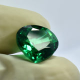 Eye-clean pear-cut green garnet held between two gloved fingers, angled to reveal its faceted brilliance