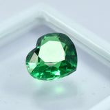 Another angle of the heart-shaped green garnet on a display lid with white borders and clear center, showcasing its shine and clarity