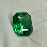 Natural green gemstone resting on a creamy fabric background, its emerald cut reflecting light in subtle soft tones