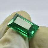 A rich green garnet gently held between two gloved fingers, showcasing its elongated emerald cut and polished facets