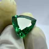 Gloved fingers holding 10.65 Ct Green Tsavorite Garnet, trillion cut, natural gemstone from Brazil