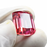 Faceted red gemstone held between white gloves on a white background