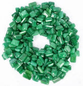 A collection of numerous tiny natural green emeralds arranged in a circular donut-like pattern, placed neatly on a white background.