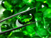 Green gemstone held by tweezers with a blurred green gemstone background