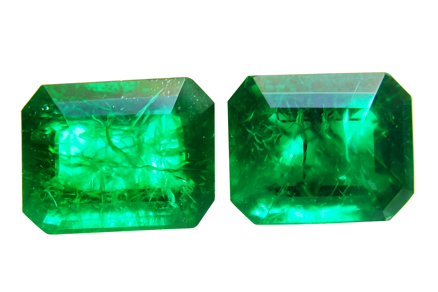 Two emerald green gemstones on a white background