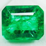  Close-up of the emerald reflecting light and casting a natural shadow on a white surface, showing depth and brilliance.
