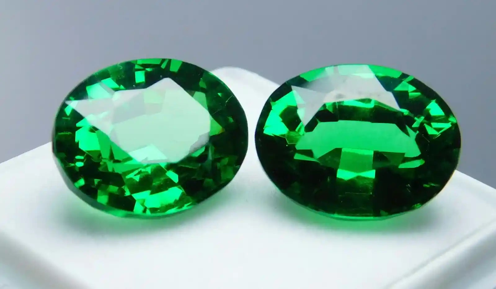 Two green gemstones on a white surface with a gray background