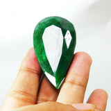 Huge pear-shaped emerald gemstone resting on fingers