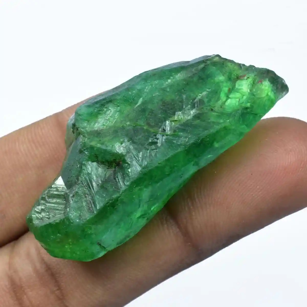 Green crystal held between fingers against a white background