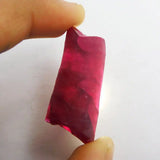 Red crystal held between two fingers against a white background