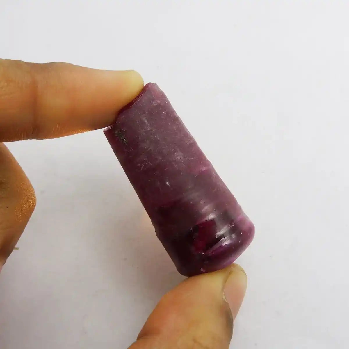 Purple cylindrical object held between fingers against a white background